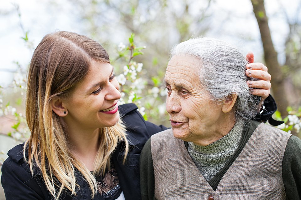 image of young woman smiling at elderly woman, speaking to one another