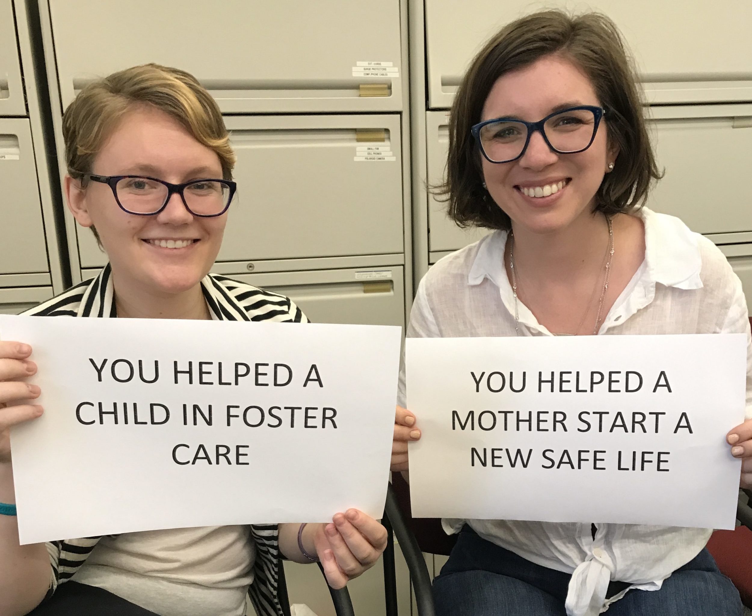 Two women holding signs, one reads "You helped a child in Foster Care" the other reads "You helped a mother start a new life"