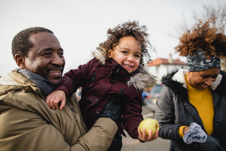 image of man holding smiling young child with an apple, and young woman