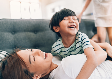 image of young woman on couch with young boy, both laughing