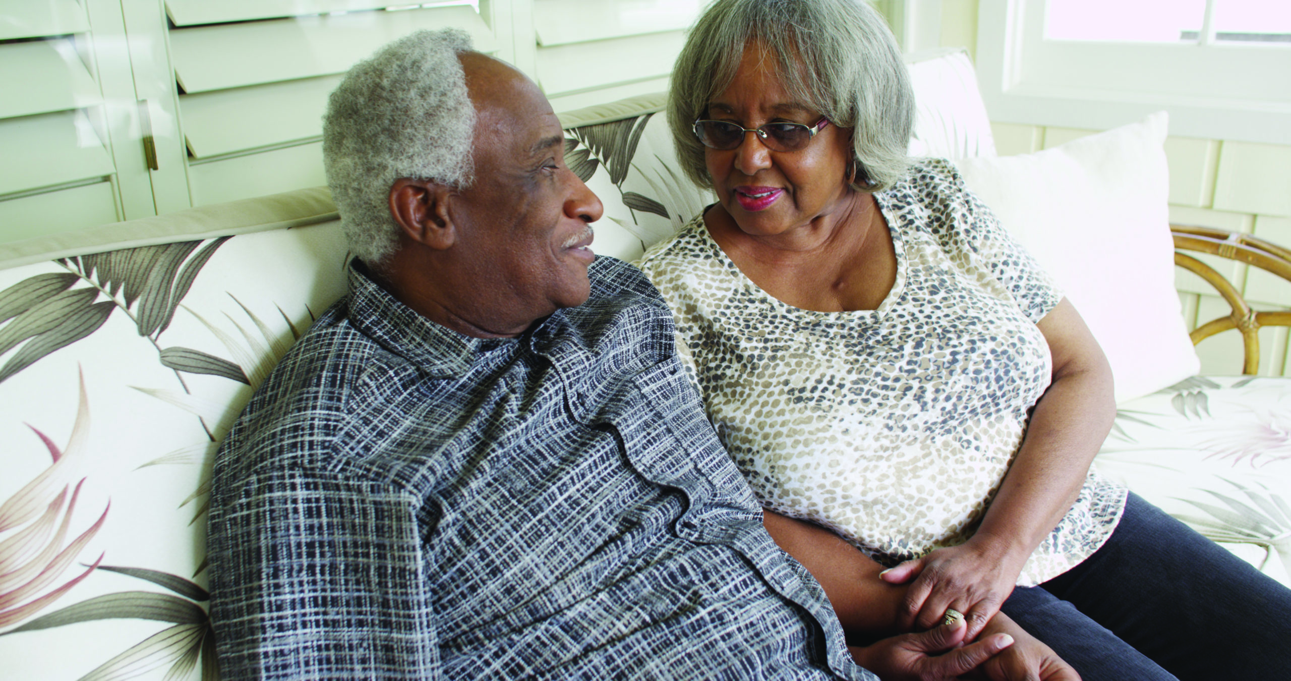 image of elderly couple holding hands, sitting on couch